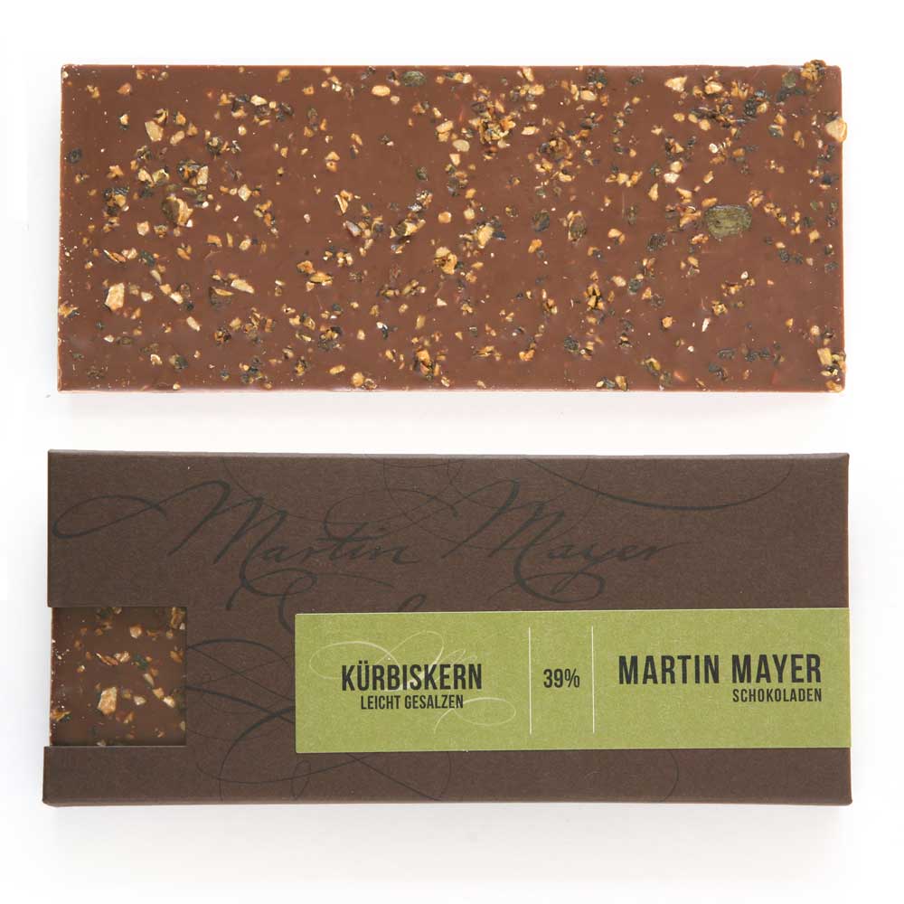 Verpackung und ausgepackte Tafel der Kürbiskernkrokant-Schokolade von Martin Mayer. Die Verpackung ist dunkelbraun mit moosgrünem Etikett und hat auf der kurzen Seite ein Sichtfenster, durch das man die Schokolade sehen kann. 