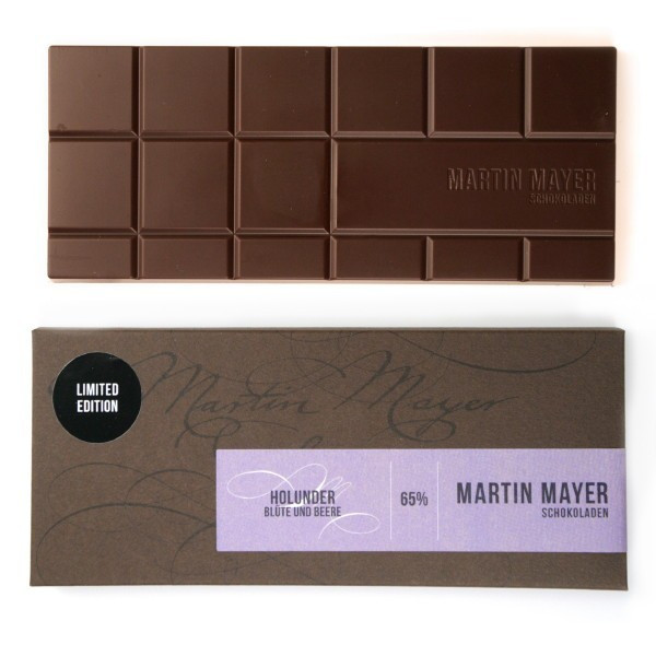 Martin Mayer gefüllte Frühlings-Schokolade mit Holunderbeere und Holunderblüte - Verpackung aus dunkelbraunem Papier mit lavendelfarbener Banderole.