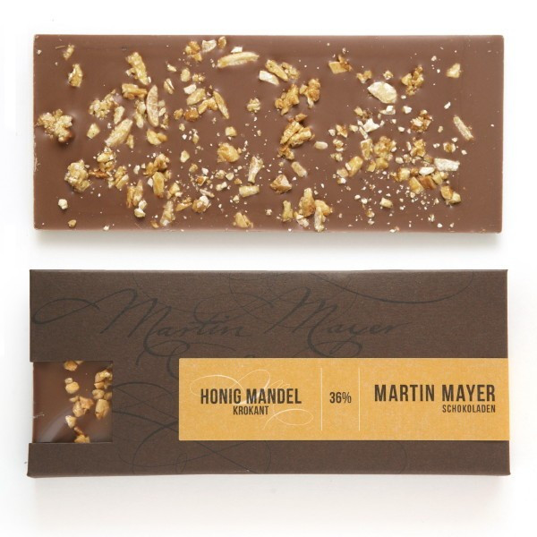 Martin Mayer Milch-Schokolade mit Mandel-Honis-Krokant  - Verpackung aus dunkelbraunem Papier mit currygelber Banderole.