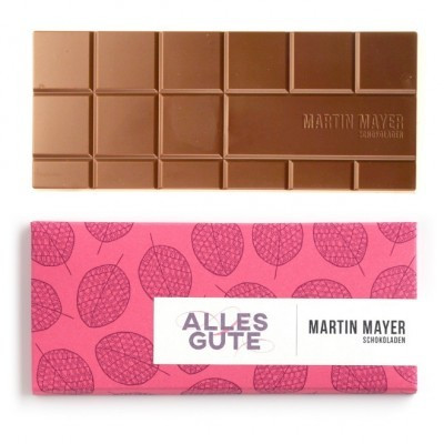 Martin Mayer Milch-Schokolade mit Himbeeren - Verpackung aus pinkem Papier mit violettem Blätter-Muster und Aufschrift „Alles Gute“